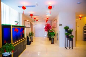 Un hall d’hôtel avec un comptoir d’accueil, des plantes en pot et des lanternes rouges.