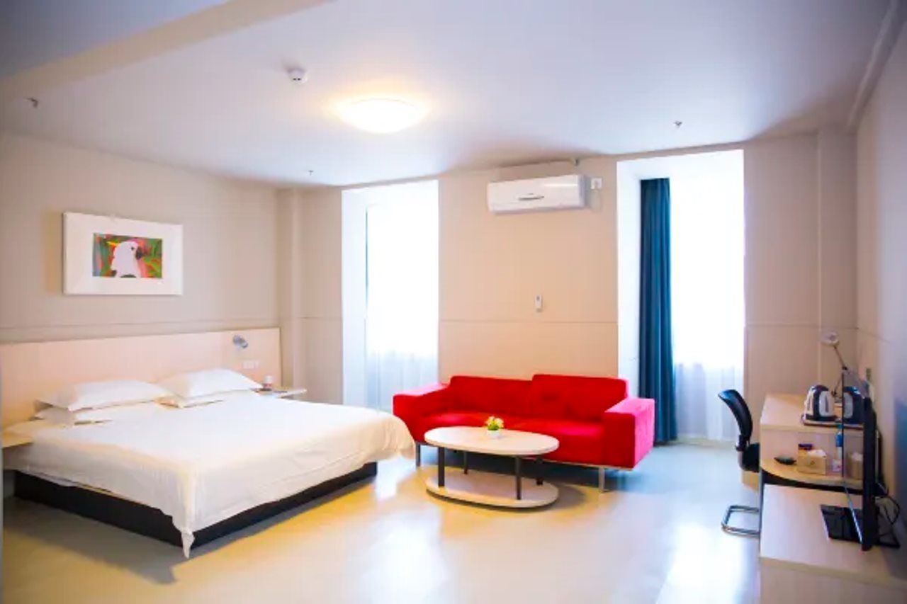A hotel room with a bed, a red sofa, a small round table, and a kitchenette area.