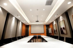 Una sala de conferencias con una larga mesa, sillas, una pantalla de proyector e iluminación empotrada en el techo.