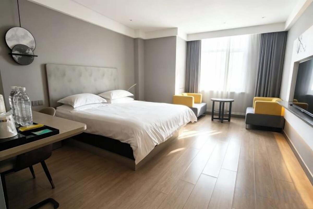 A hotel room with a bed, a desk, a chair, a TV, and a window with curtains.