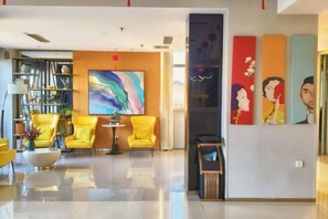 A modern lobby with yellow chairs, a large abstract painting, and three vertical artworks.