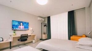 Une chambre d’hôtel avec deux lits, un bureau avec une chaise, un téléviseur fixé au mur et une fenêtre avec des rideaux.