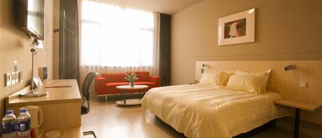 A hotel room with a bed, a desk, a chair, a TV, and a window with curtains.