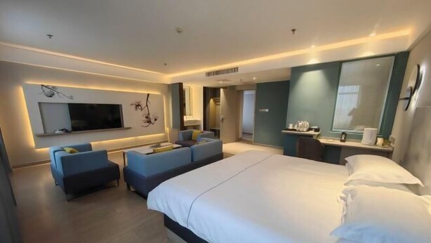 Une chambre d’hôtel moderne dotée d’un grand lit, d’un téléviseur à écran plat fixé au mur, d’un coin salon avec des canapés et d’une petite table avec une lampe.
