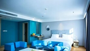 Une chambre d’hôtel moderne avec un lit, des fauteuils bleus, une petite table et une table de chevet.