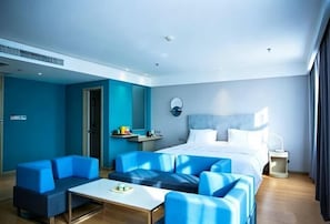 Una habitación de hotel moderna con una cama, asientos azules, una mesita y una mesita de noche.