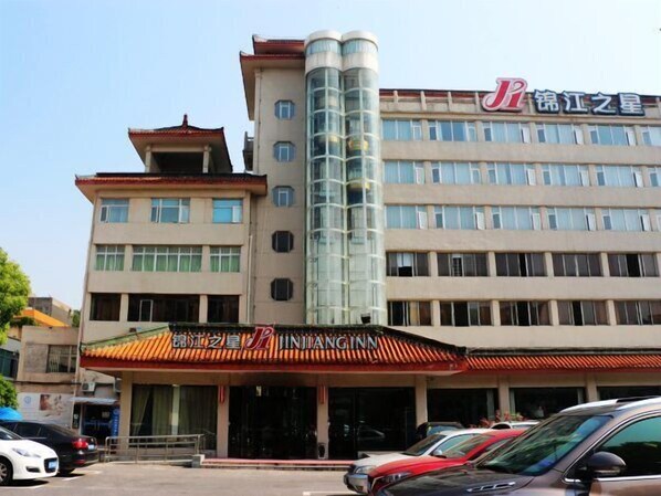 A hotel with a traditional Chinese architectural style, featuring a prominent curved glass tower and a red awning with the hotel name.