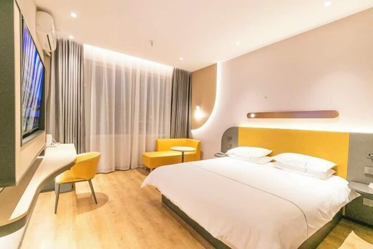 A modern hotel room with a curved bed, a small round table, and a TV mounted on the wall.