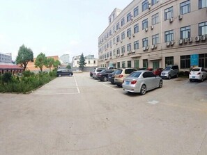 A parking lot with several cars parked in front of a multi-story building with air conditioning units. - Jinjiang Inn Zhuji Datang Hotel (Shaoxing)