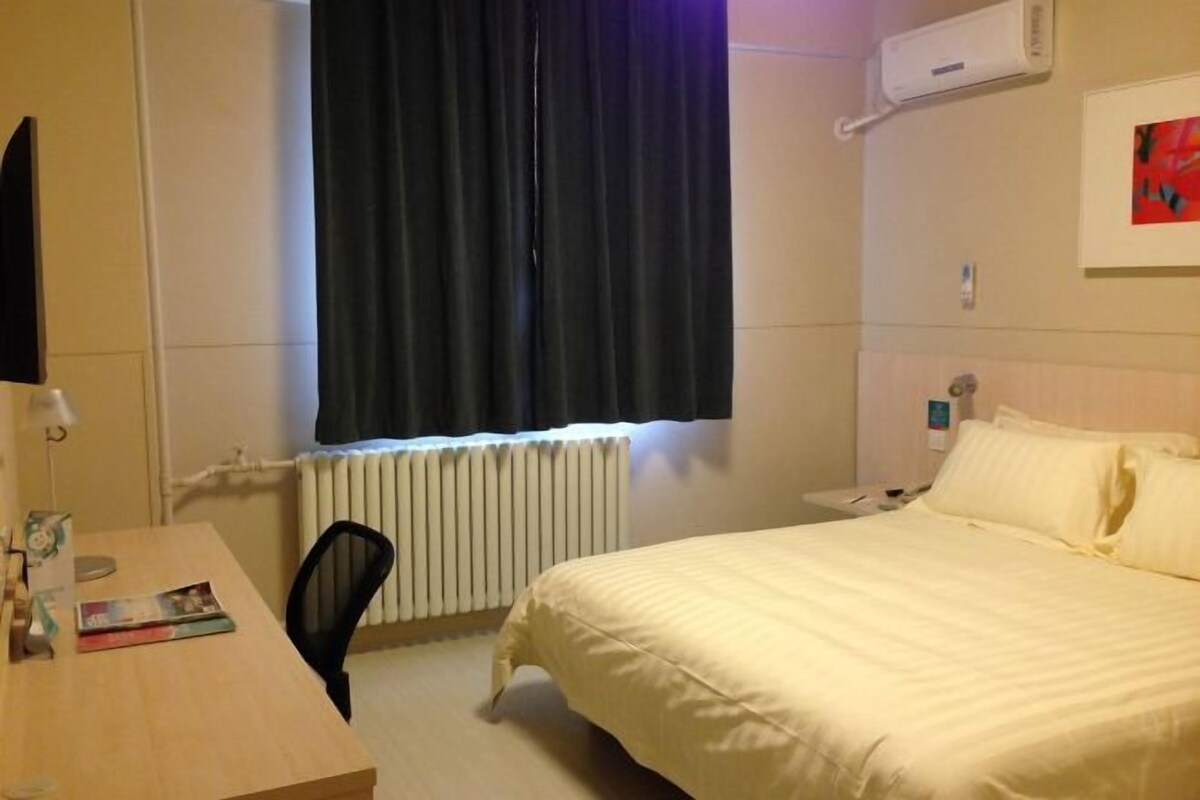 Ein Hotelzimmer mit einem Bett, einem Schreibtisch, einem Stuhl, einem Heizkörper und einem Fenster mit Vorhängen.