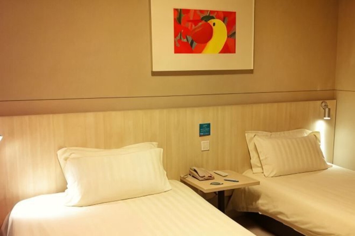 Una habitación de hotel con dos camas, una mesita de noche con un teléfono y un cuadro en la pared.
