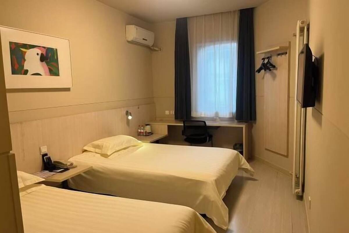 Habitación de hotel con dos camas, un escritorio con silla, una ventana con cortinas y un perchero.
