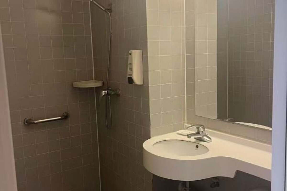 Un baño con ducha, lavabo, espejo y dispensador de jabón.