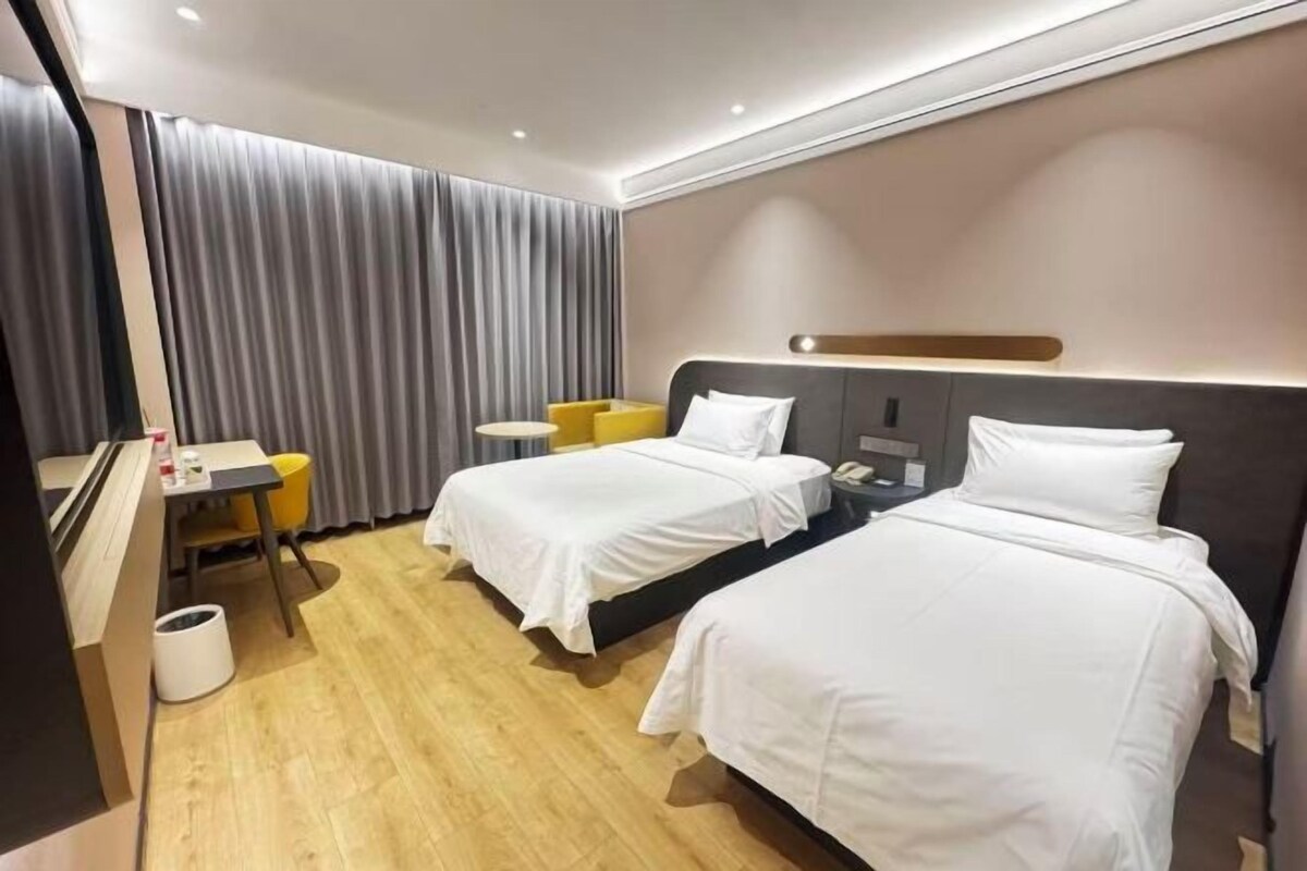 Ein Hotelzimmer mit zwei Betten, einem Schreibtisch, einem Sessel und einem großen Fenster mit Vorhängen.