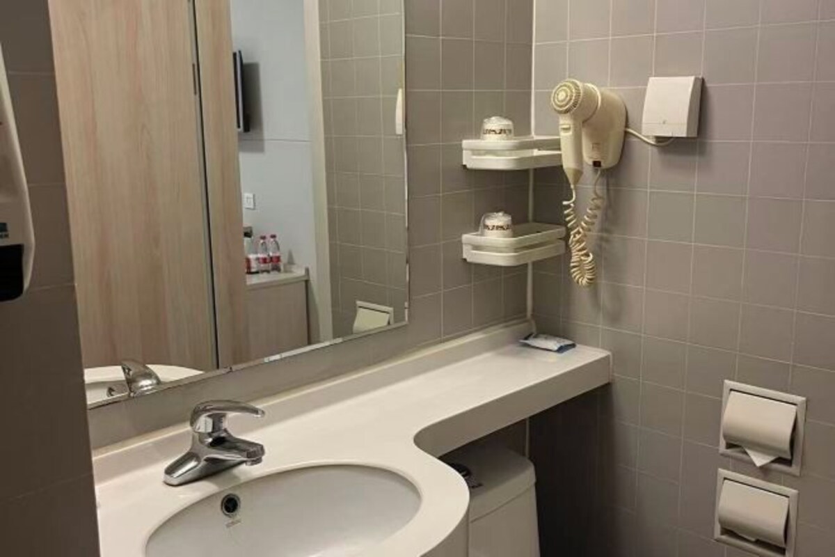 Un baño con lavamanos, espejo, secador de pelo y dispensador de toallas.