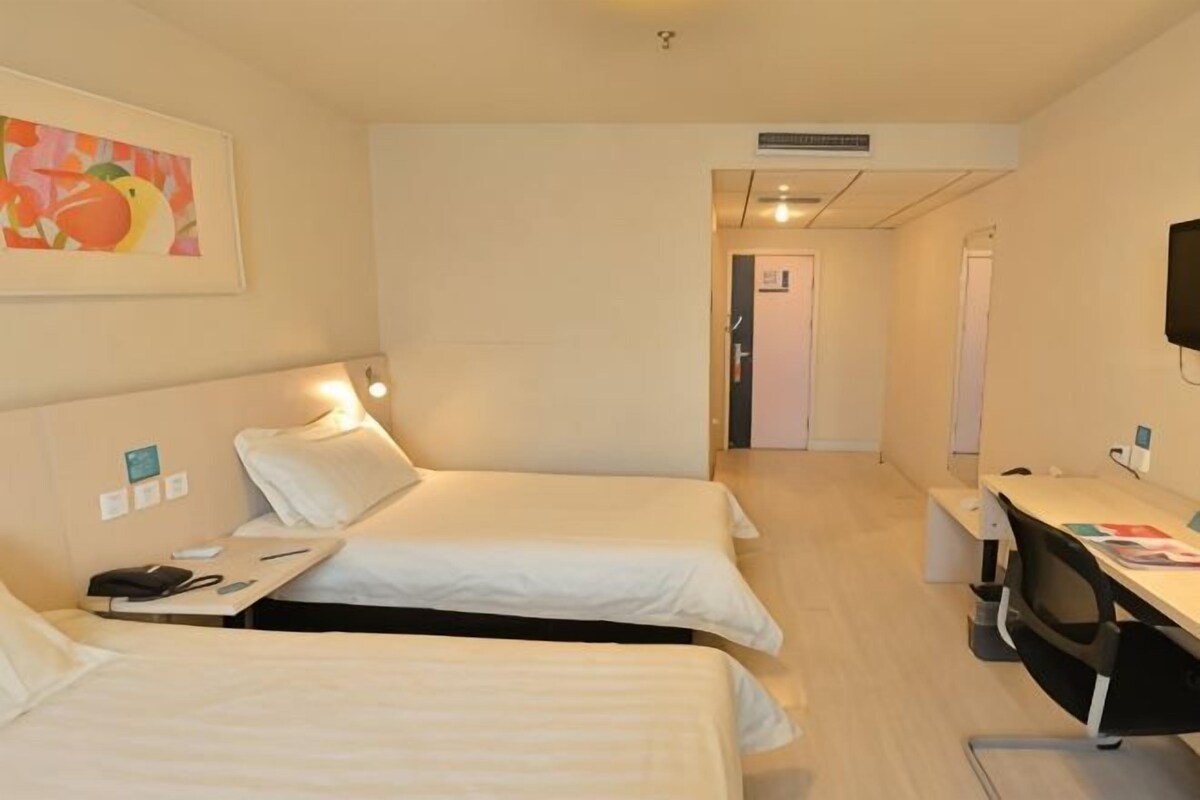 Ein Hotelzimmer mit zwei Betten, einem Schreibtisch, einem Sessel, einem Fernseher und einer Tür zu einem weiteren Raum.