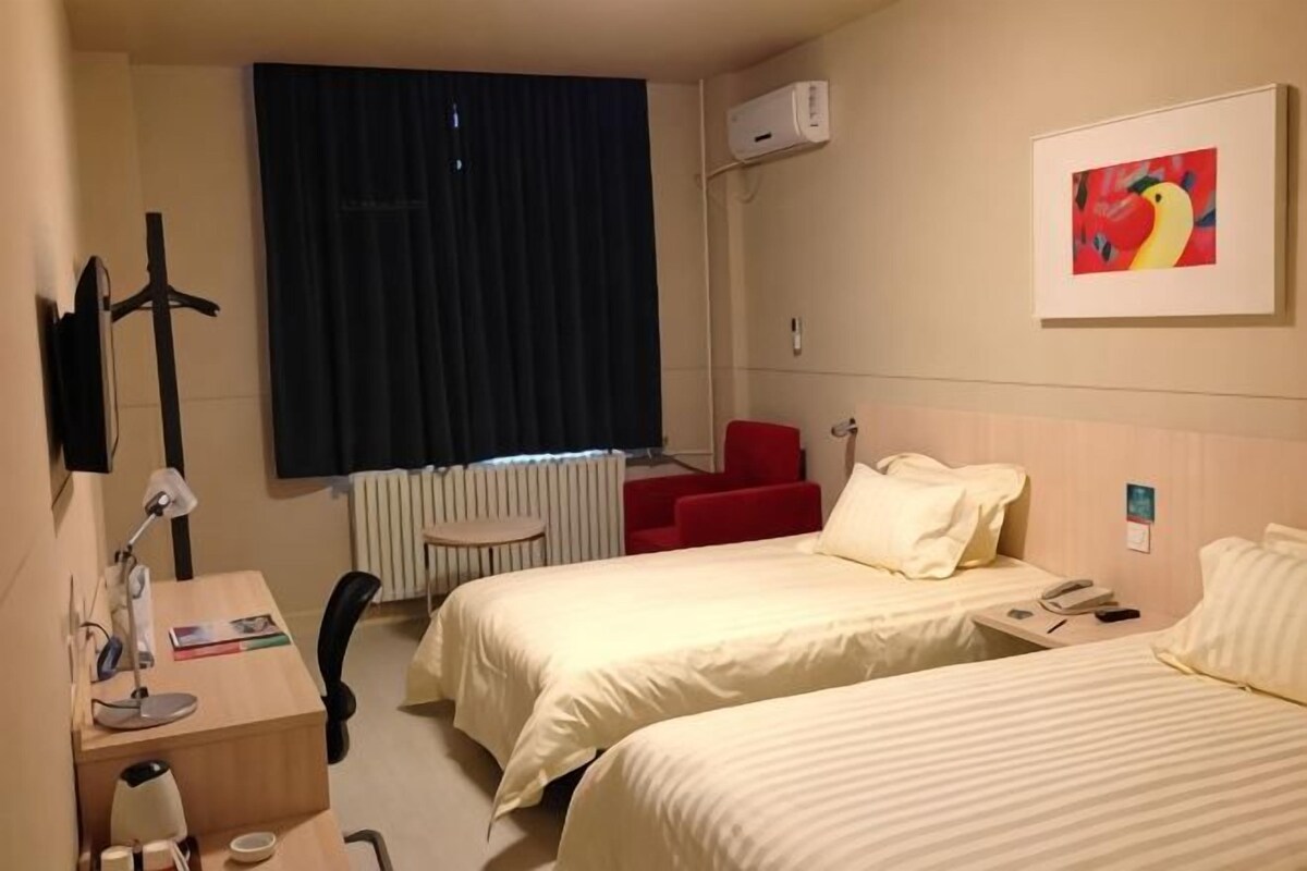 Ein Hotelzimmer mit zwei Betten, einem Schreibtisch, einem Stuhl, einer Heizung, einem Fernseher und einem Bild an der Wand.