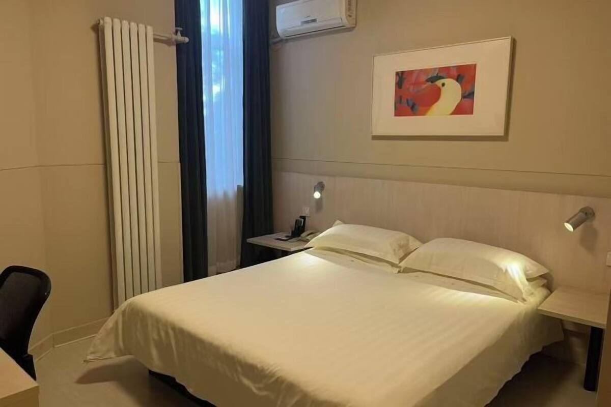 Una habitación de hotel con cama, mesita de noche, lámpara y un cuadro en la pared.