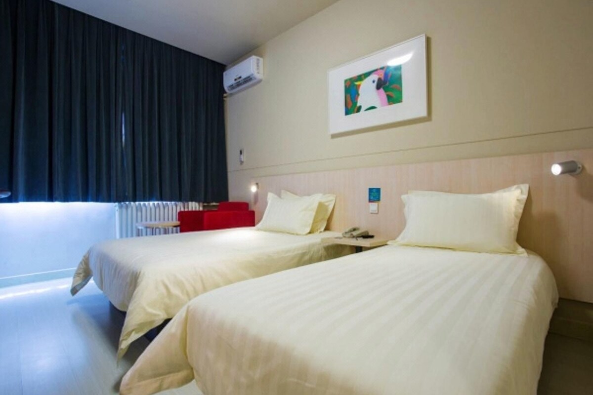 Habitación de hotel con dos camas, un sofá rojo, un equipo de aire acondicionado y un cuadro en la pared.
