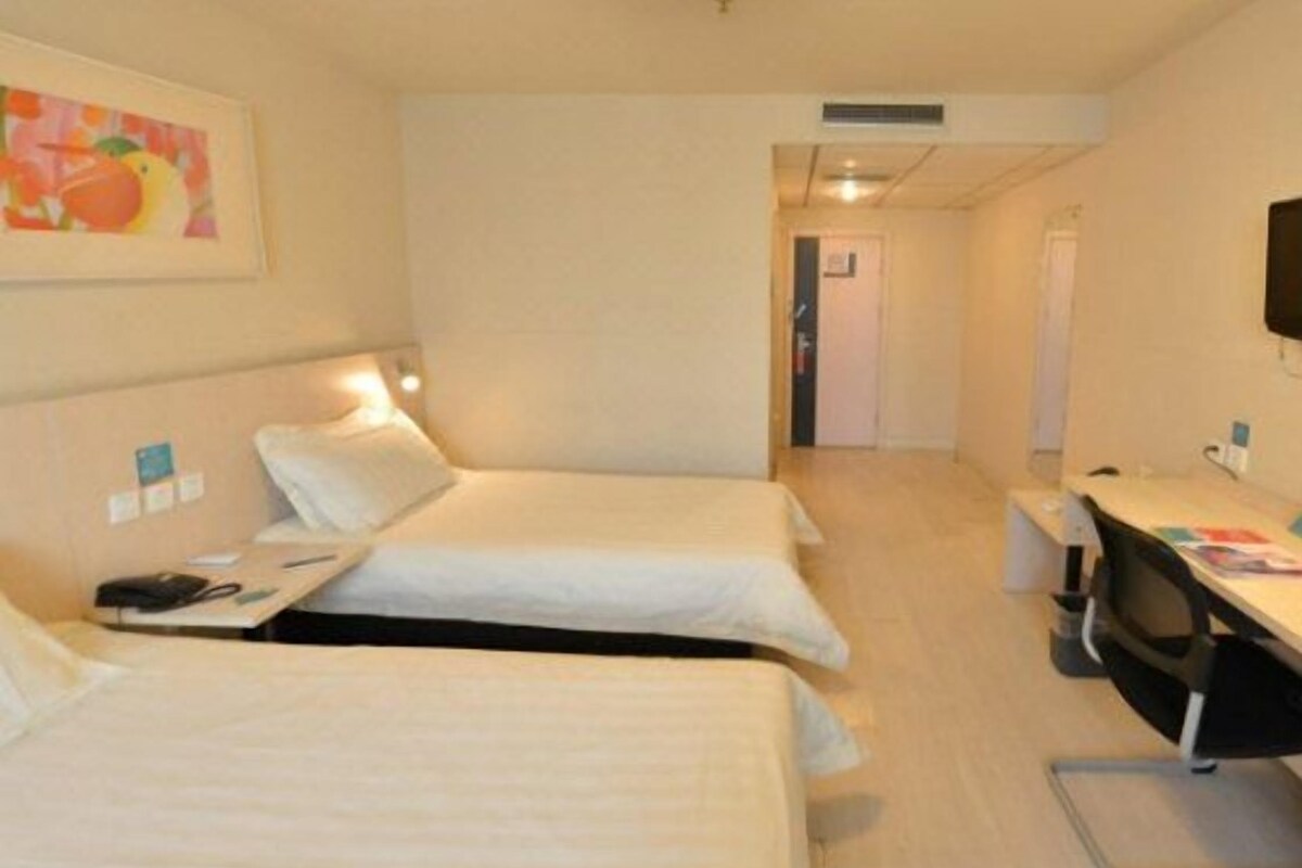 Habitación de hotel con dos camas, un escritorio y una silla. Se observa una puerta que conduce a otra habitación y un televisor fijado a la pared.