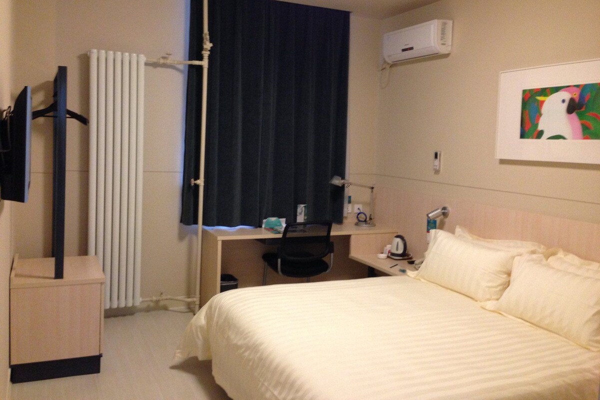 Habitación de hotel con cama, escritorio, silla, radiador, aire acondicionado y un cuadro en la pared.