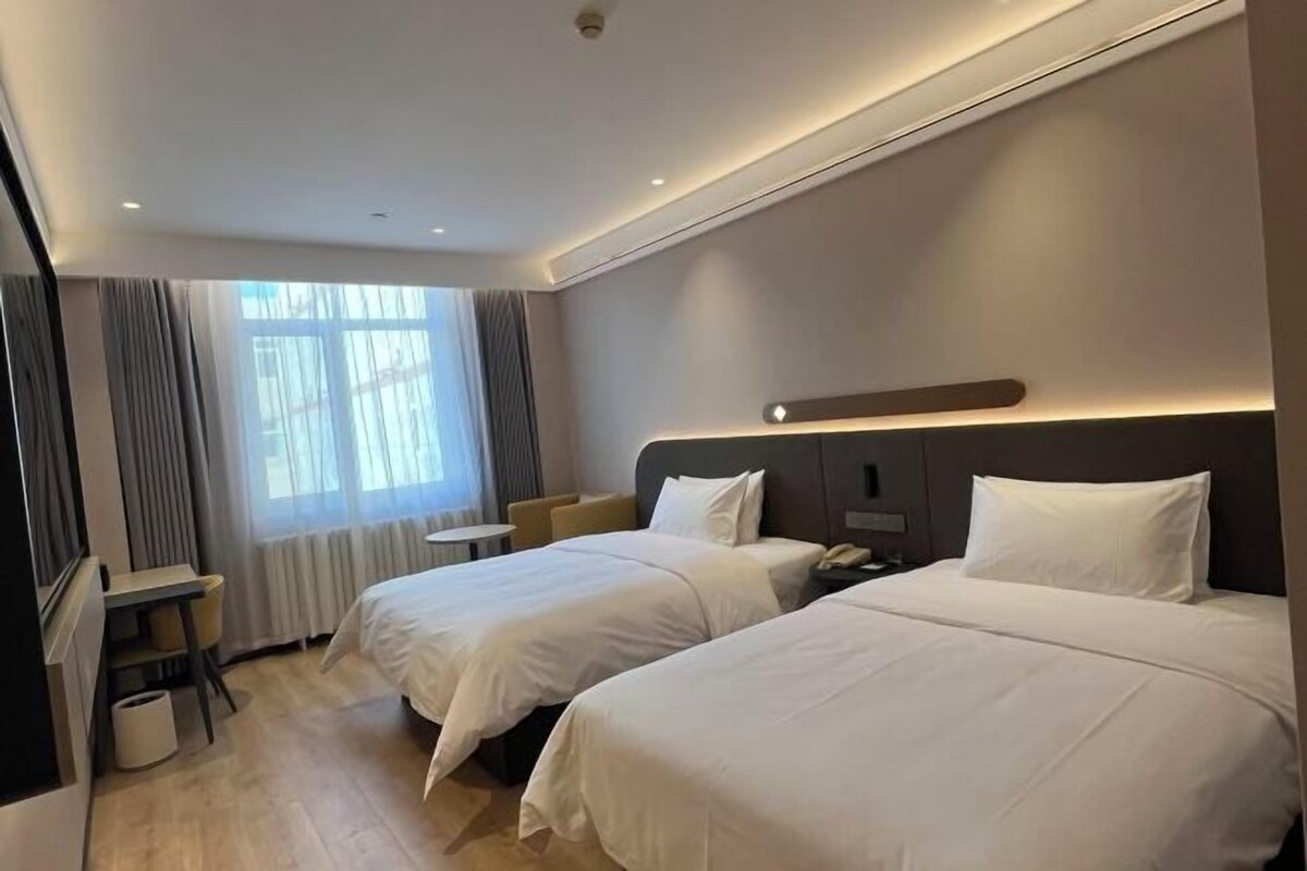 Ein Hotelzimmer mit zwei Betten, einem Schreibtisch und einem Fenster mit Vorhängen.