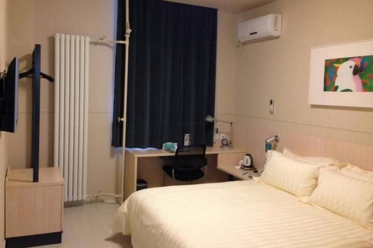 Habitación de hotel con cama, escritorio, silla, radiador, aire acondicionado y un cuadro en la pared.