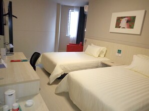 Une chambre d’hôtel avec deux lits, un bureau avec une lampe, une chaise et une fenêtre avec des rideaux.