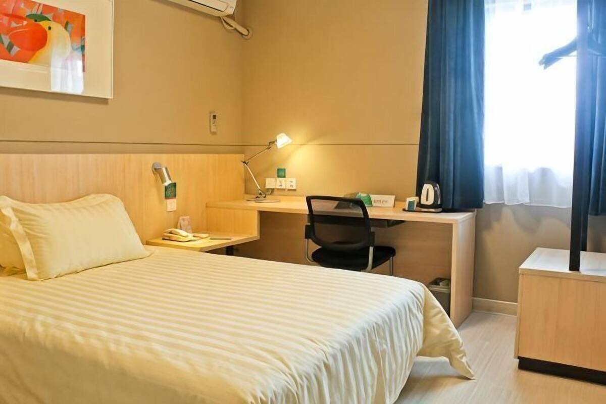 Een hotelkamer met een bed, bureau, stoel en een raam met gordijnen.