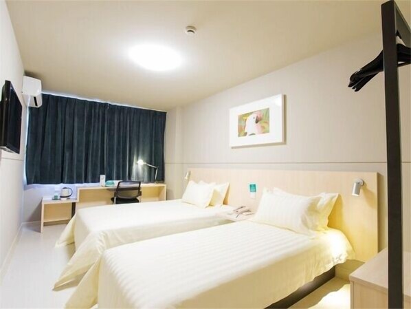 A hotel room with two beds, a desk, a chair, a lamp, and a painting on the wall.