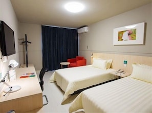 A hotel room with two beds, a desk with a lamp, a chair, a TV, and a painting on the wall.