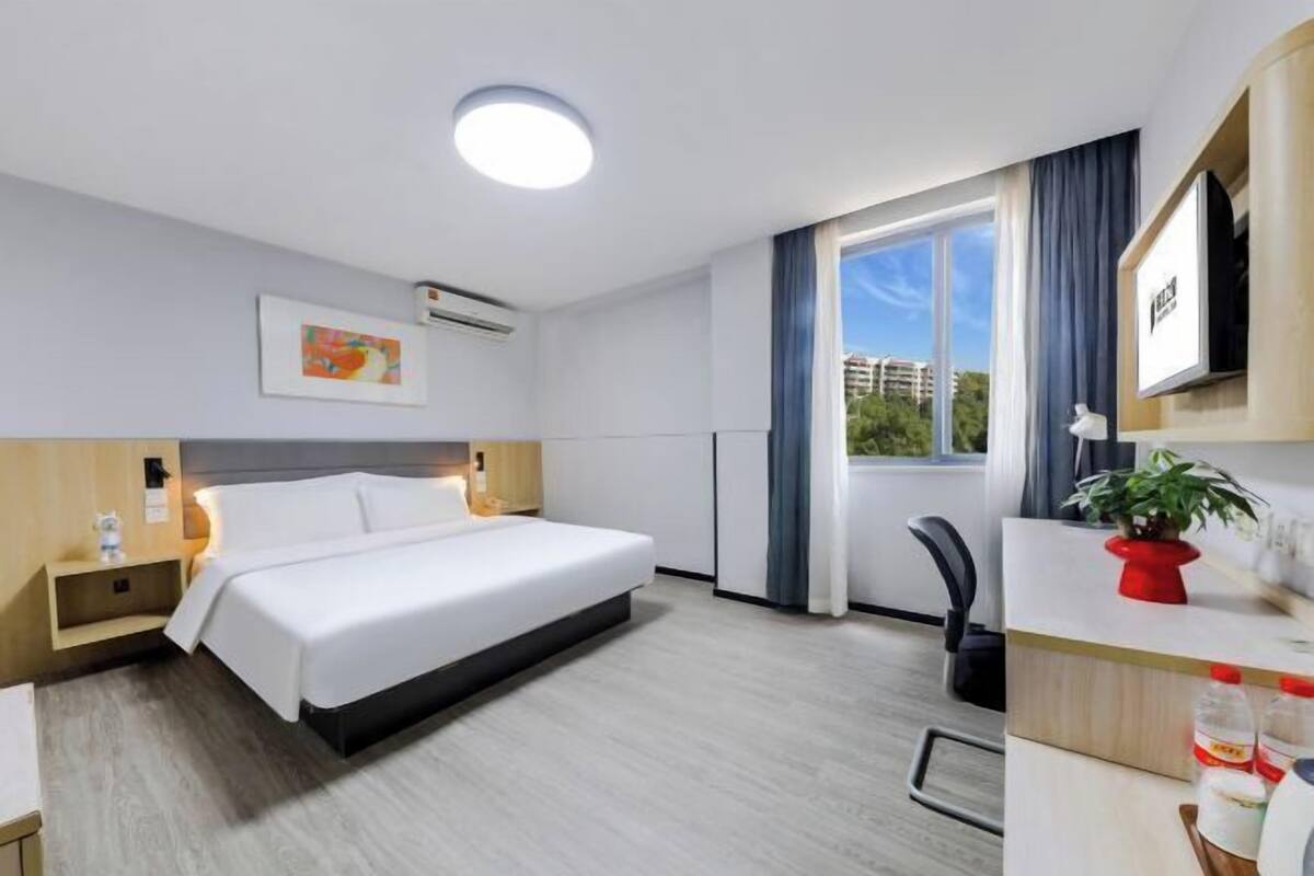 Une chambre d’hôtel avec un lit, une table de chevet, une télévision et une fenêtre avec des rideaux.