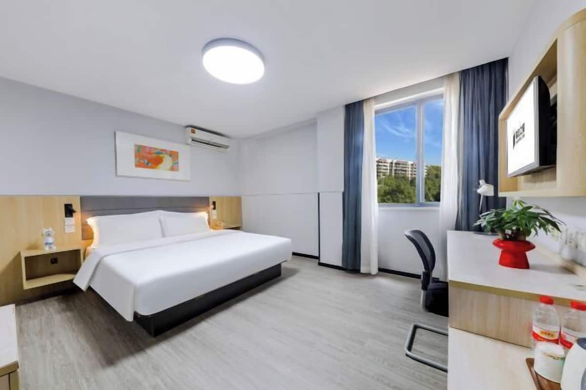 Une chambre d’hôtel équipée d’un lit, d’une table de chevet, d’un bureau, d’une chaise et d’une fenêtre donnant sur un paysage agréable.