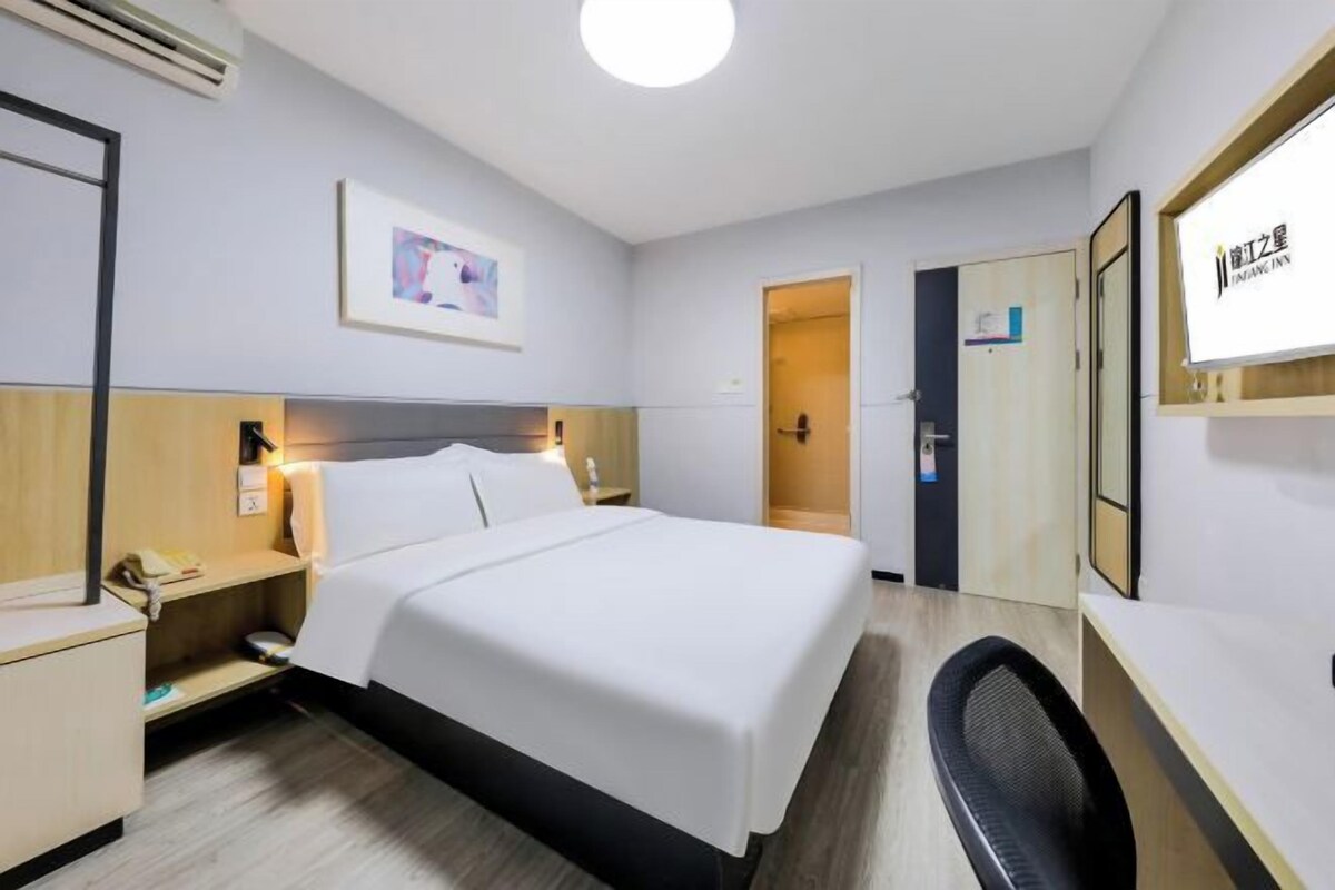 Una habitación de hotel con cama, mesita de noche, lámpara y escritorio con silla.