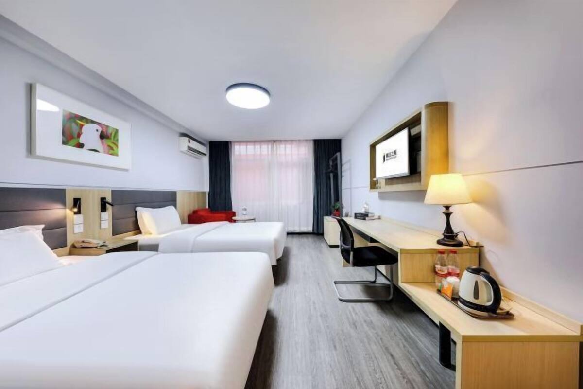 Une chambre d’hôtel avec deux lits, un bureau, une chaise, une lampe et un tableau au mur.