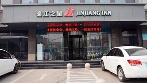 Entree van een JINJIANG INN hotel, met een moderne gevel, een glazen ingang en twee witte auto's ervoor geparkeerd.