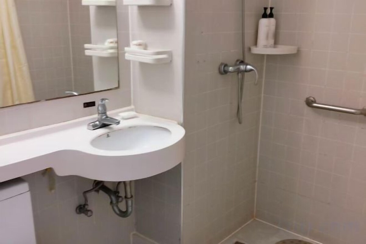 Ein Badezimmer mit weißem Waschbecken, einem Spiegel, einer Dusche und einer Haltestange.