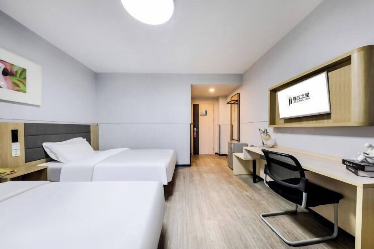 Une chambre d’hôtel avec deux lits, un bureau, une chaise, une télévision et un miroir.