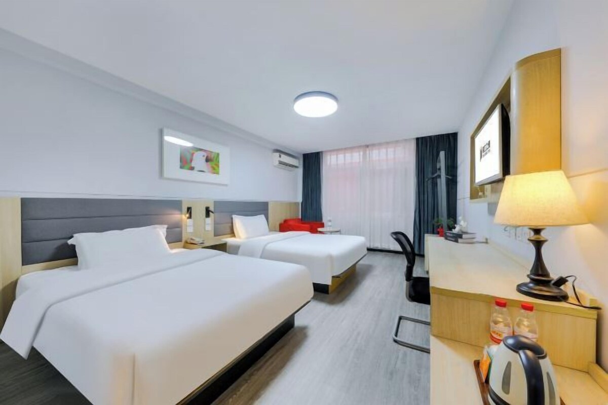A hotel room with two beds, a desk, a chair, a lamp, and a window with curtains.