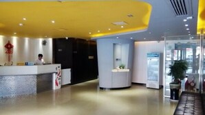 Een moderne hotelontvangsthal met een gebogen receptiebalie, een receptionist en een glazen scheidingswand.
