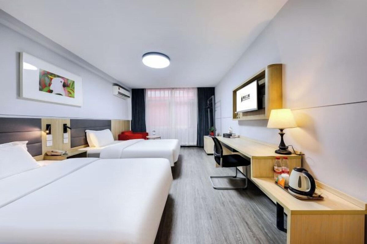 Quarto de hotel com duas camas, uma escrivaninha, uma cadeira, um abajur e uma televisão.