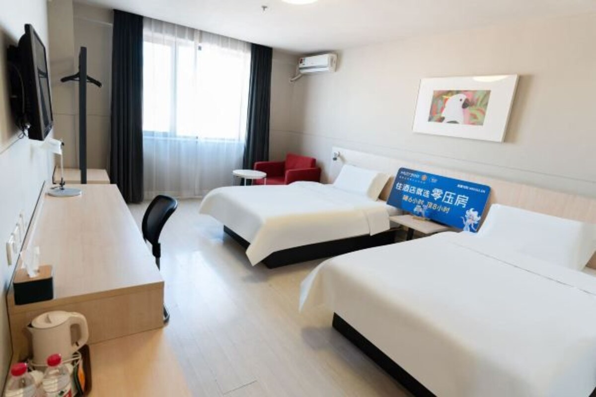 A hotel room with two beds, a desk, a chair, a TV, and a window with curtains.