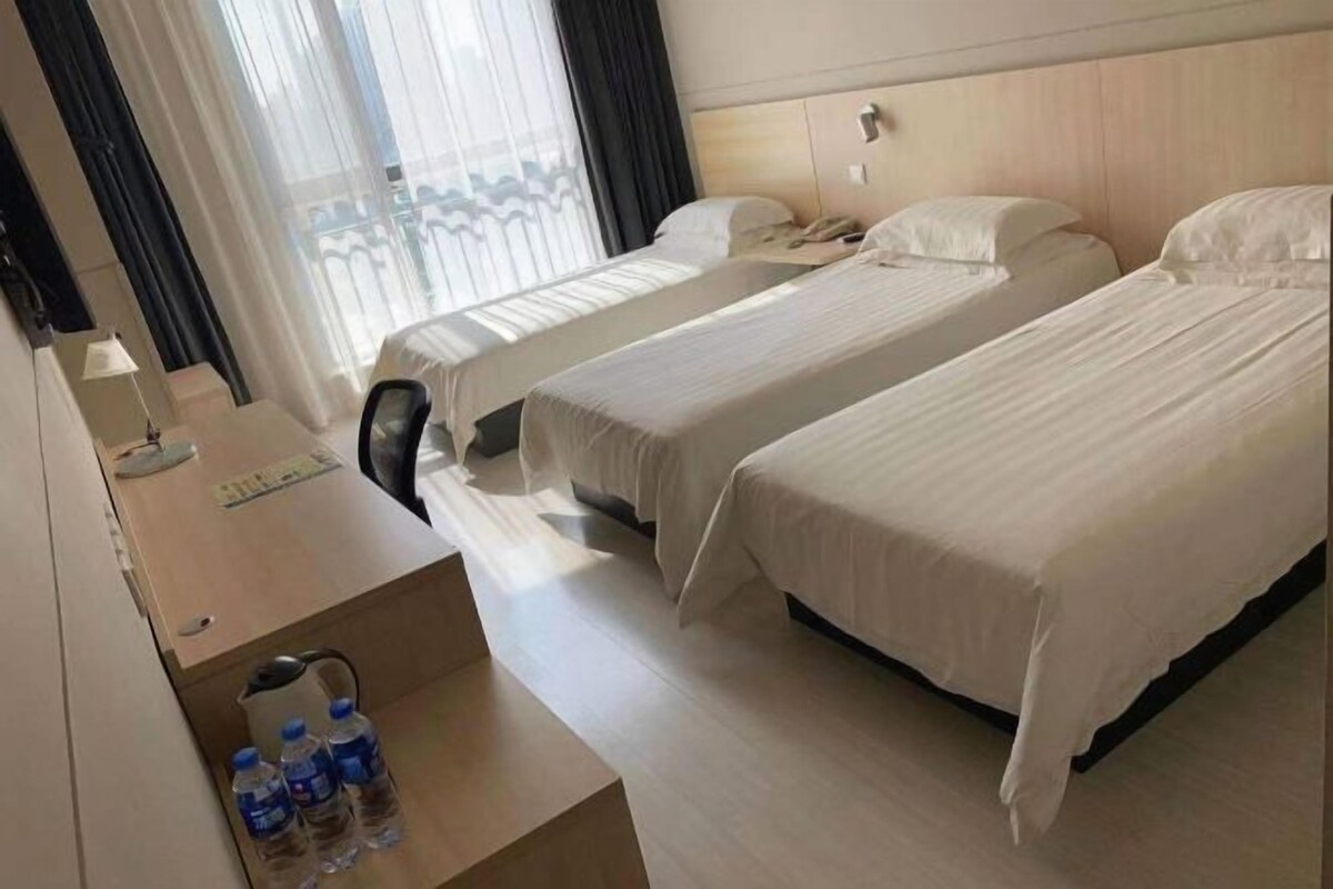 A hotel room with two beds, a desk with a lamp, and a window with curtains.