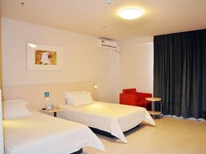 Ein Hotelzimmer mit zwei Betten, einem roten Sessel, einem kleinen Tisch und einem Bild an der Wand.
