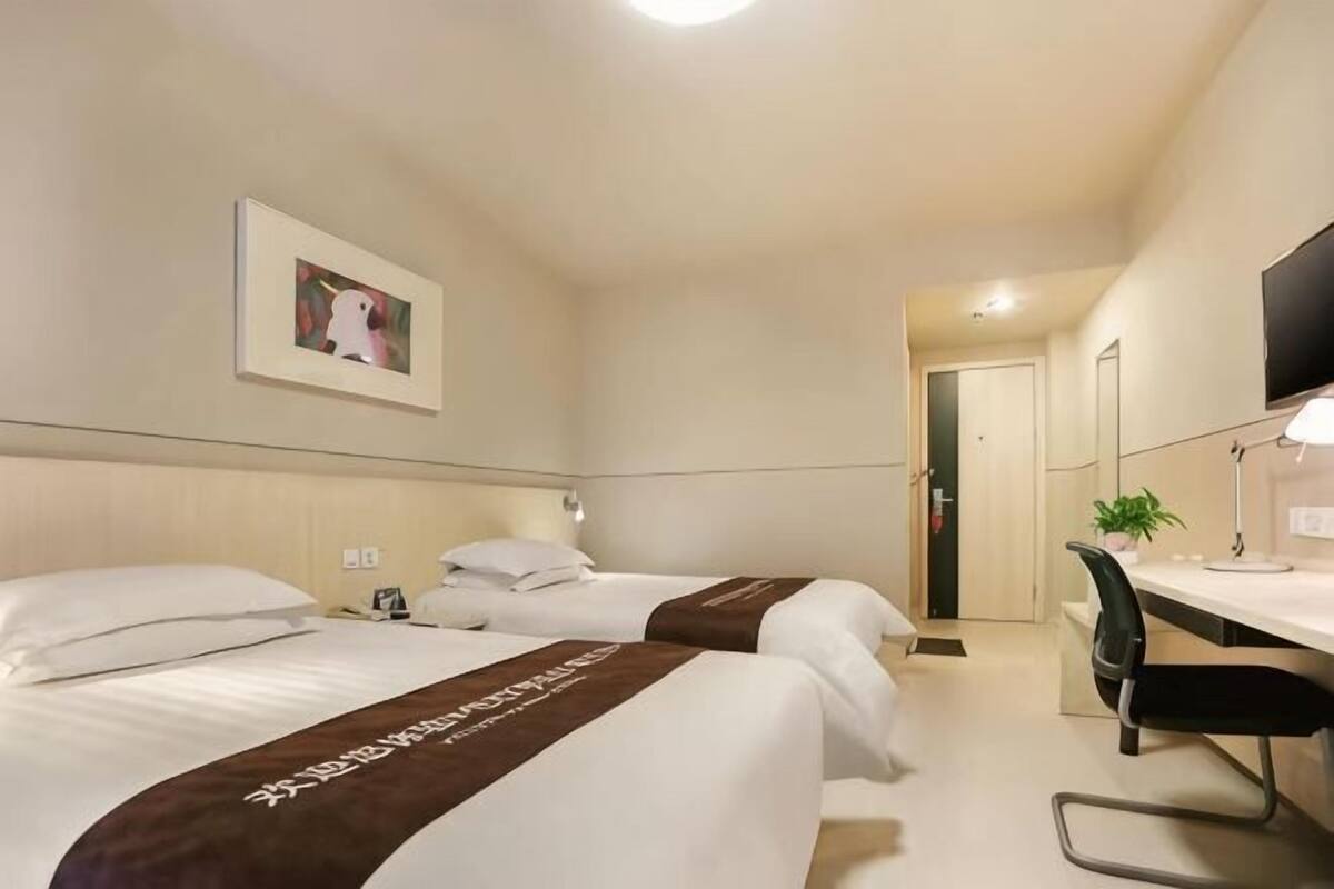 Ein Hotelzimmer mit zwei Betten, einem Schreibtisch, einem Sessel, einem Fernseher und einem gerahmten Bild an der Wand.