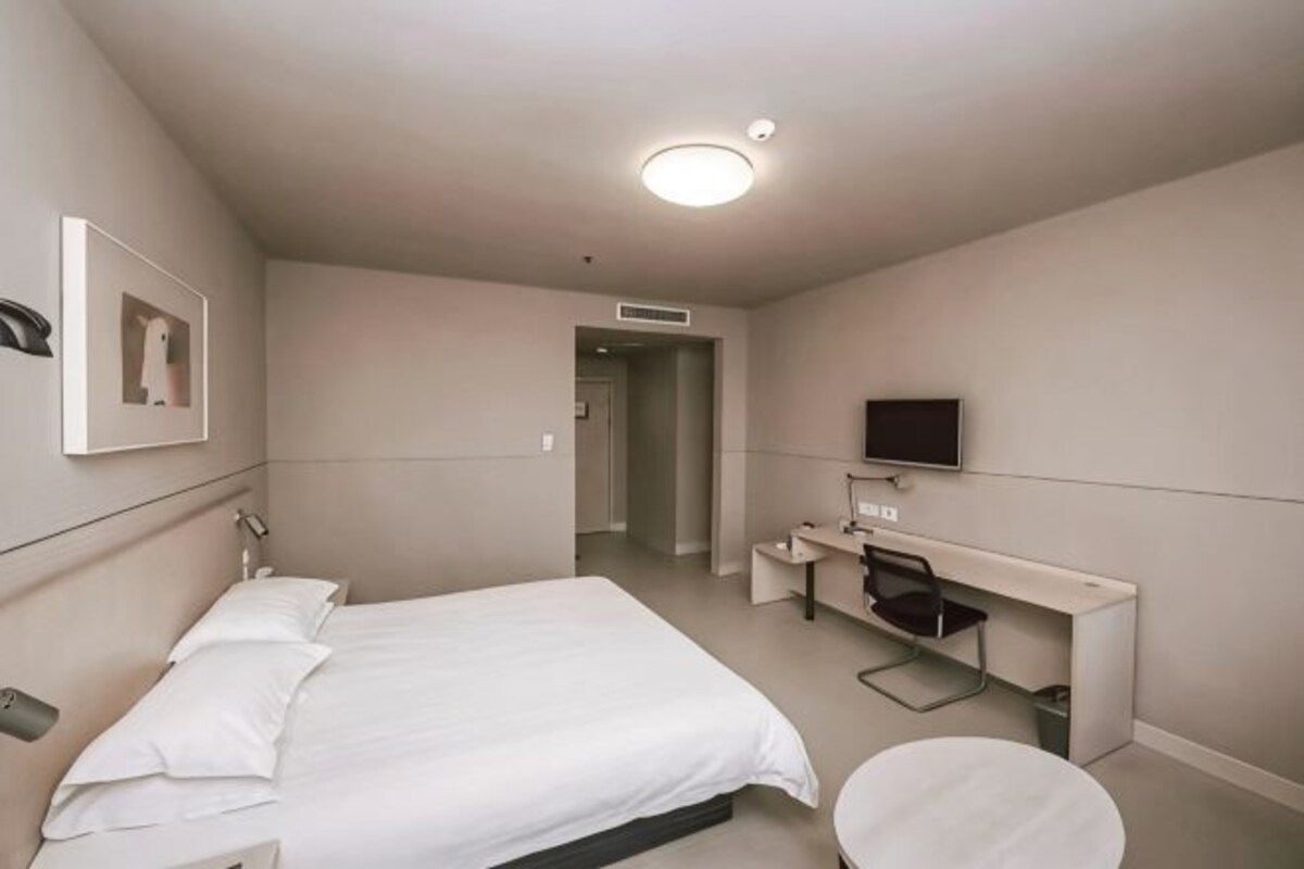 A hotel room with a bed, desk, chair, TV, and a door leading to another room.