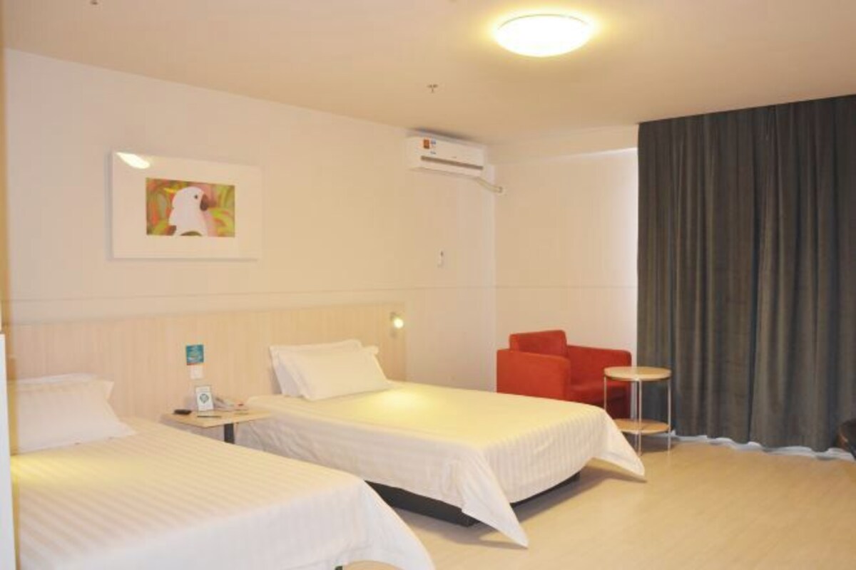 A hotel room with two beds, a red chair, a small table, and a painting on the wall.