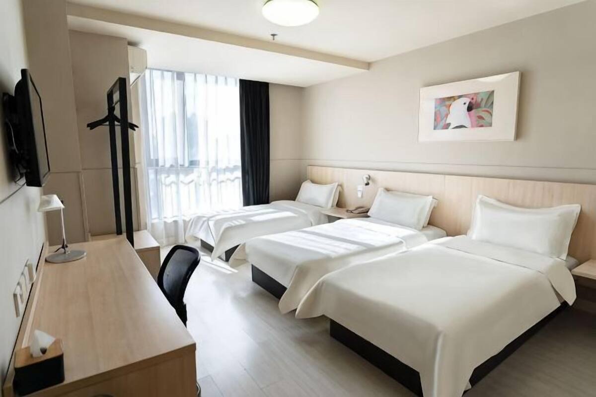 Ein Hotelzimmer mit zwei Betten, einem Schreibtisch, einem Stuhl, einem Fernseher und einem Fenster mit Vorhängen.