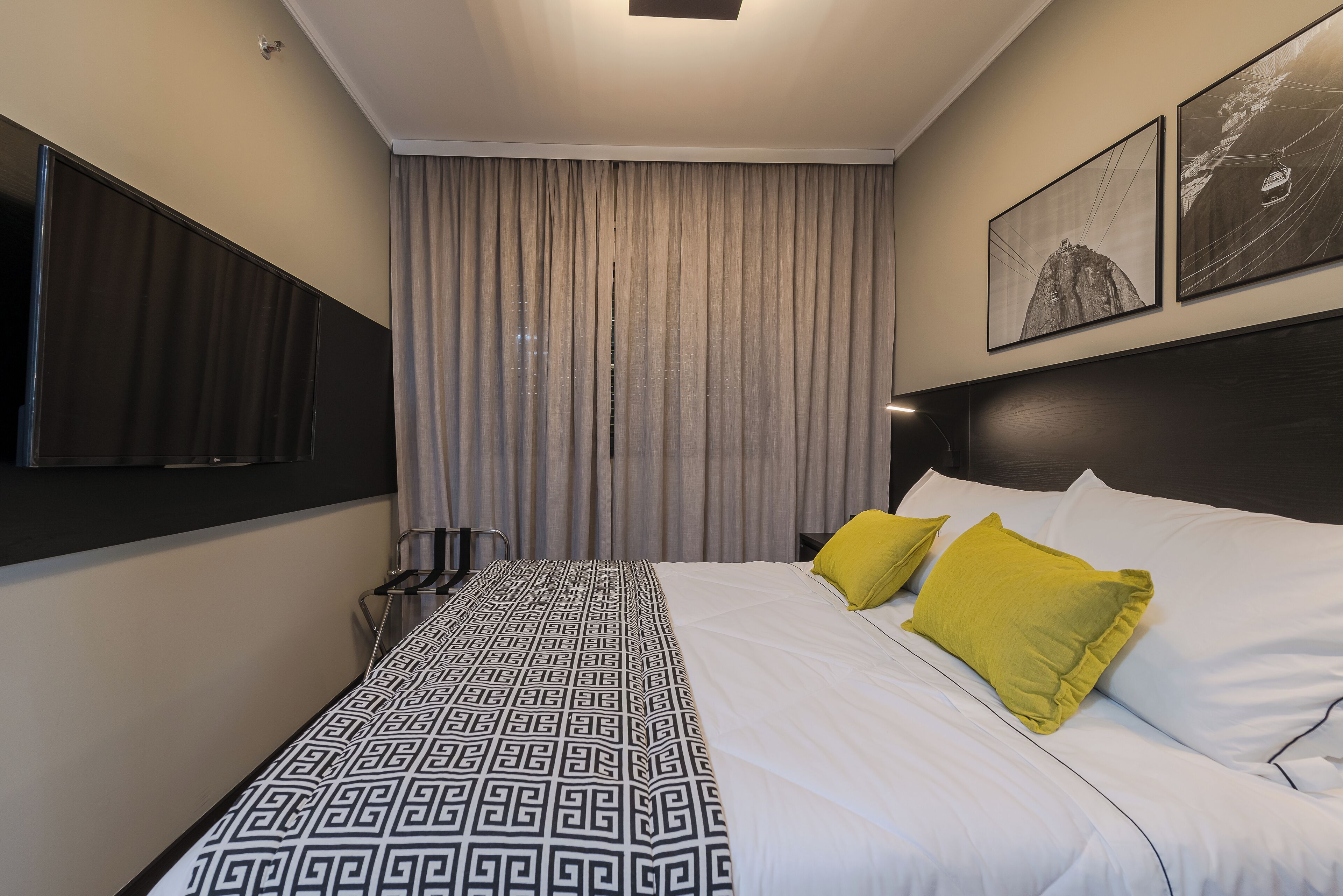 A hotel room with a large bed, a TV mounted on the wall, and a window with curtains.