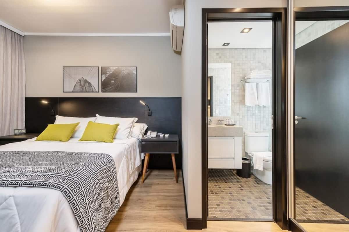 Habitación de hotel con cama, mesita de noche y baño visible a través de una puerta abierta.